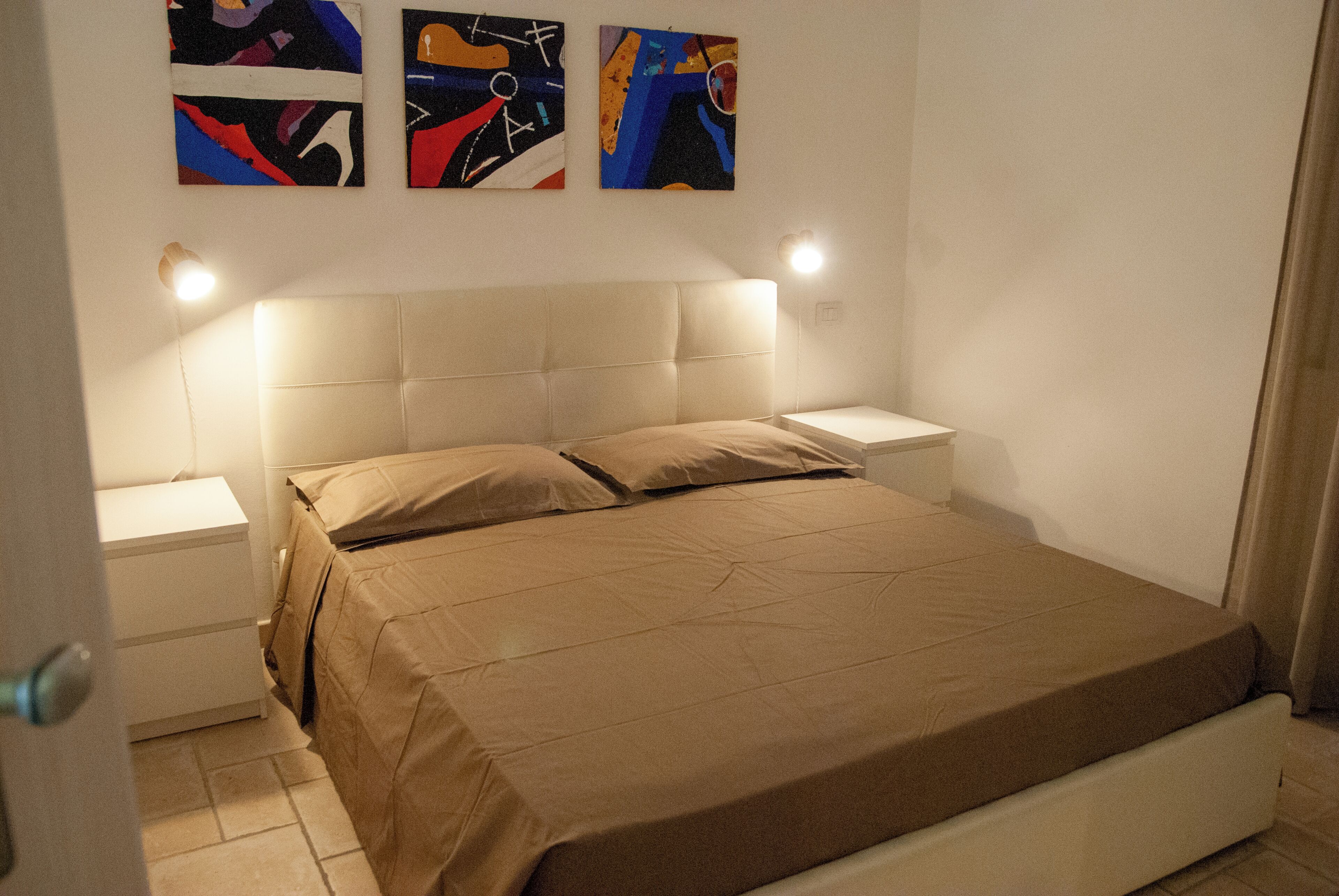 Ein Schlafzimmer mit Bett, Nachttischen und abstrakten Wandbildern.