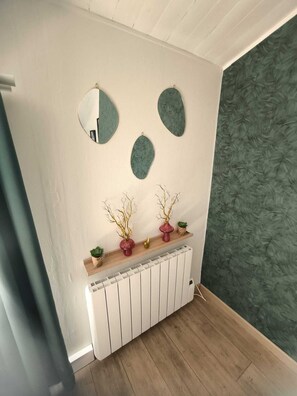 Ein Zimmer mit einem Heizkörper, einem Regal mit Dekoration und zwei Wandspiegeln.