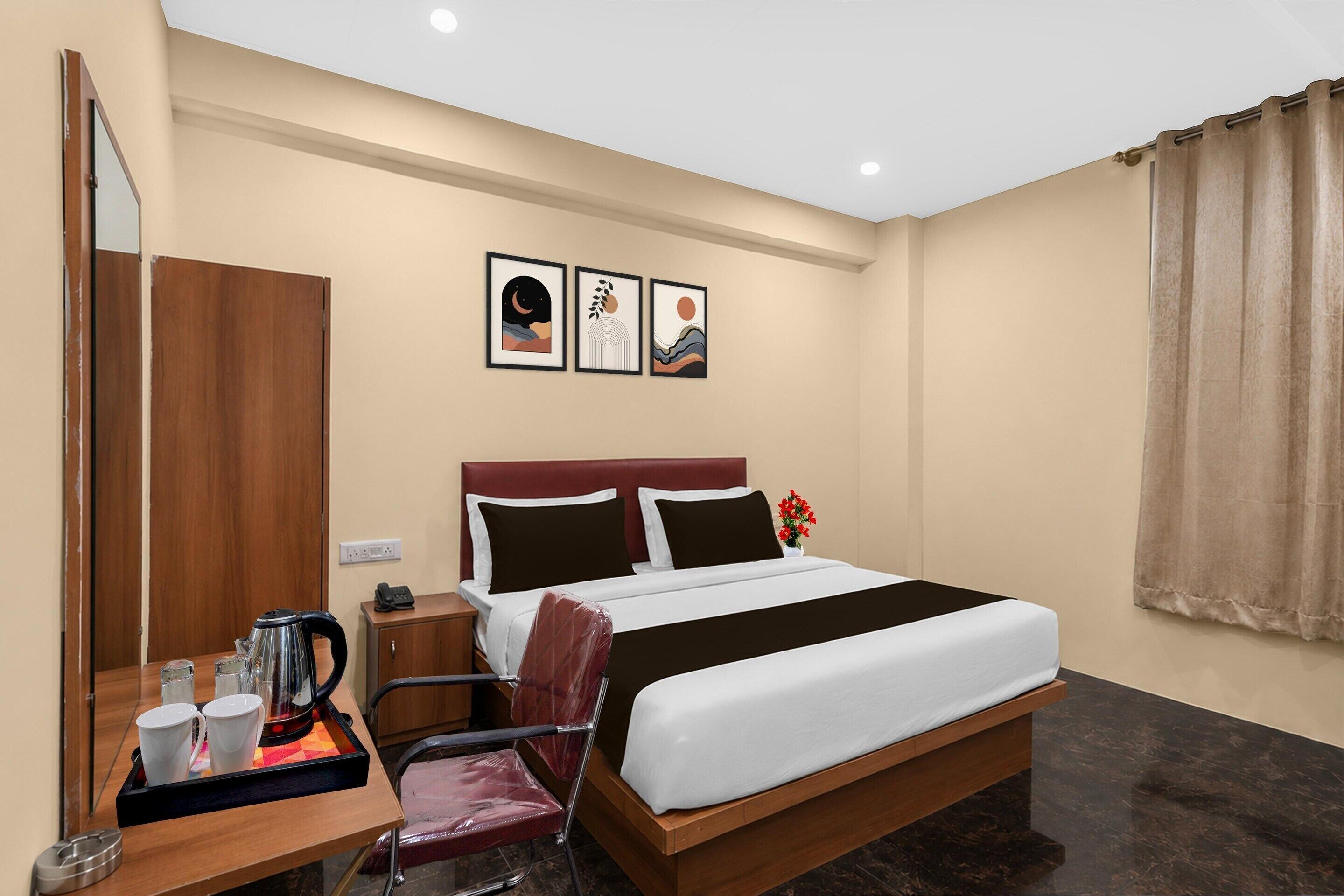 A hotel room with a bed, a desk with a kettle, cups, and a chair.