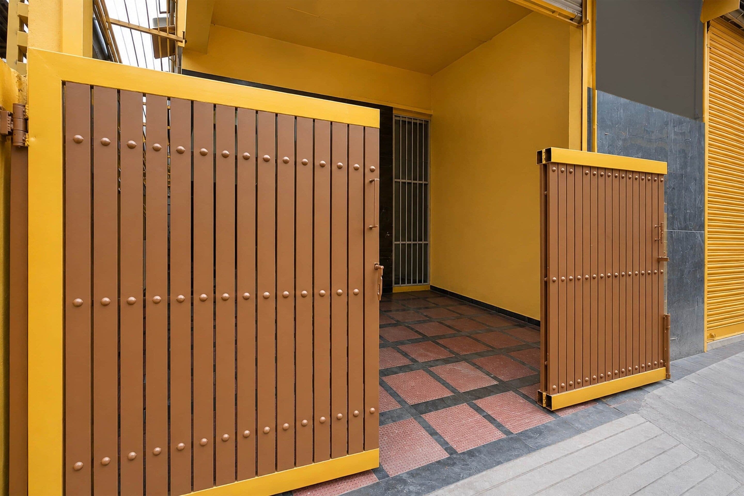 A gated entrance with a yellow and brown color scheme, a tiled floor, and a metal gate.