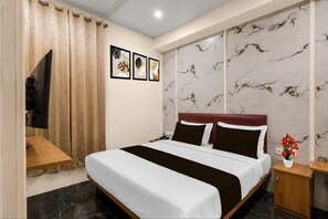 A hotel room with a bed, a TV, a nightstand, a vase with flowers, and a marble-patterned wall. - Townhouse Mantri Square Metro Station (Bengaluru)