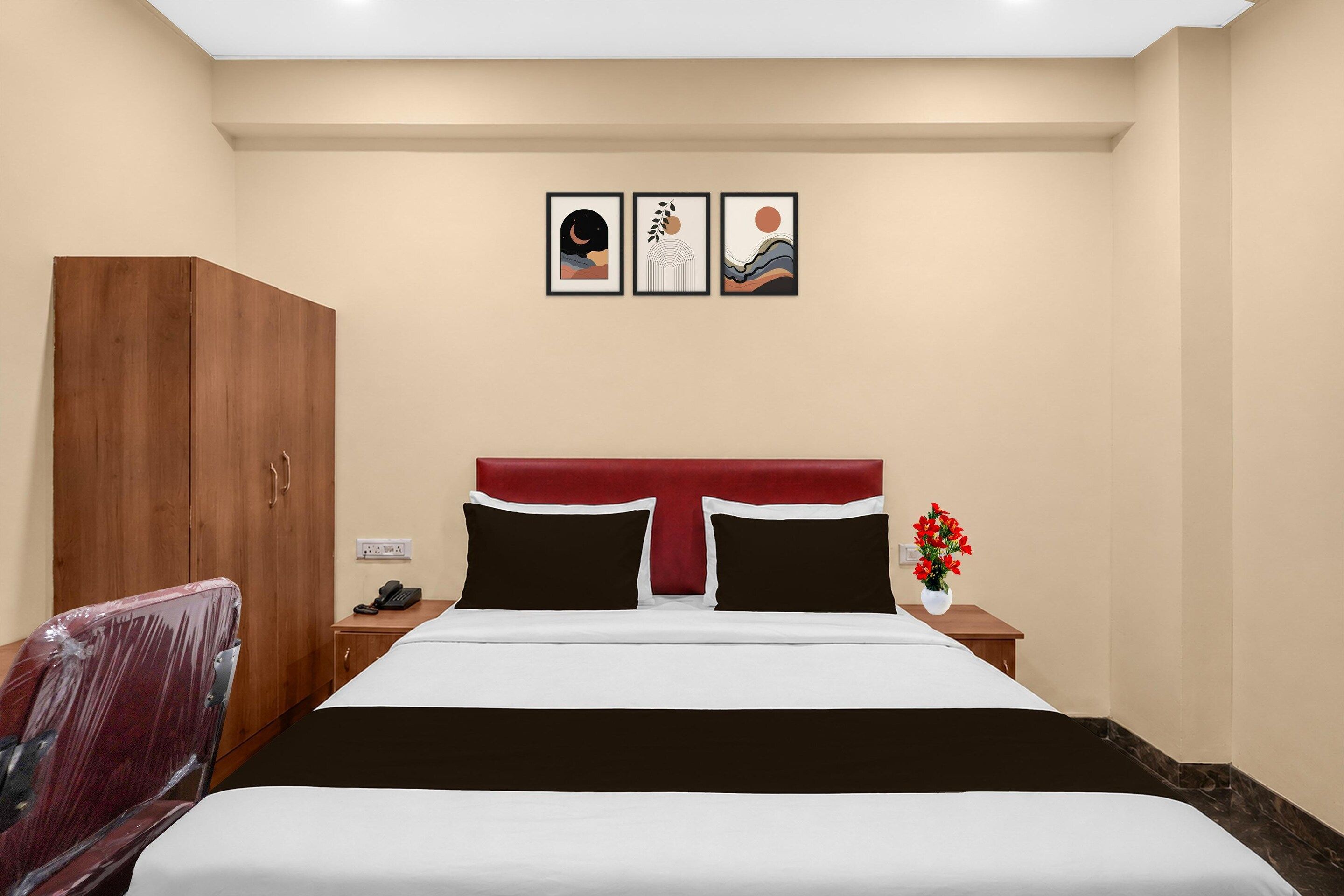Una habitación de hotel con una cama, un armario, una mesita de noche con un teléfono y una pared con tres cuadros enmarcados.
