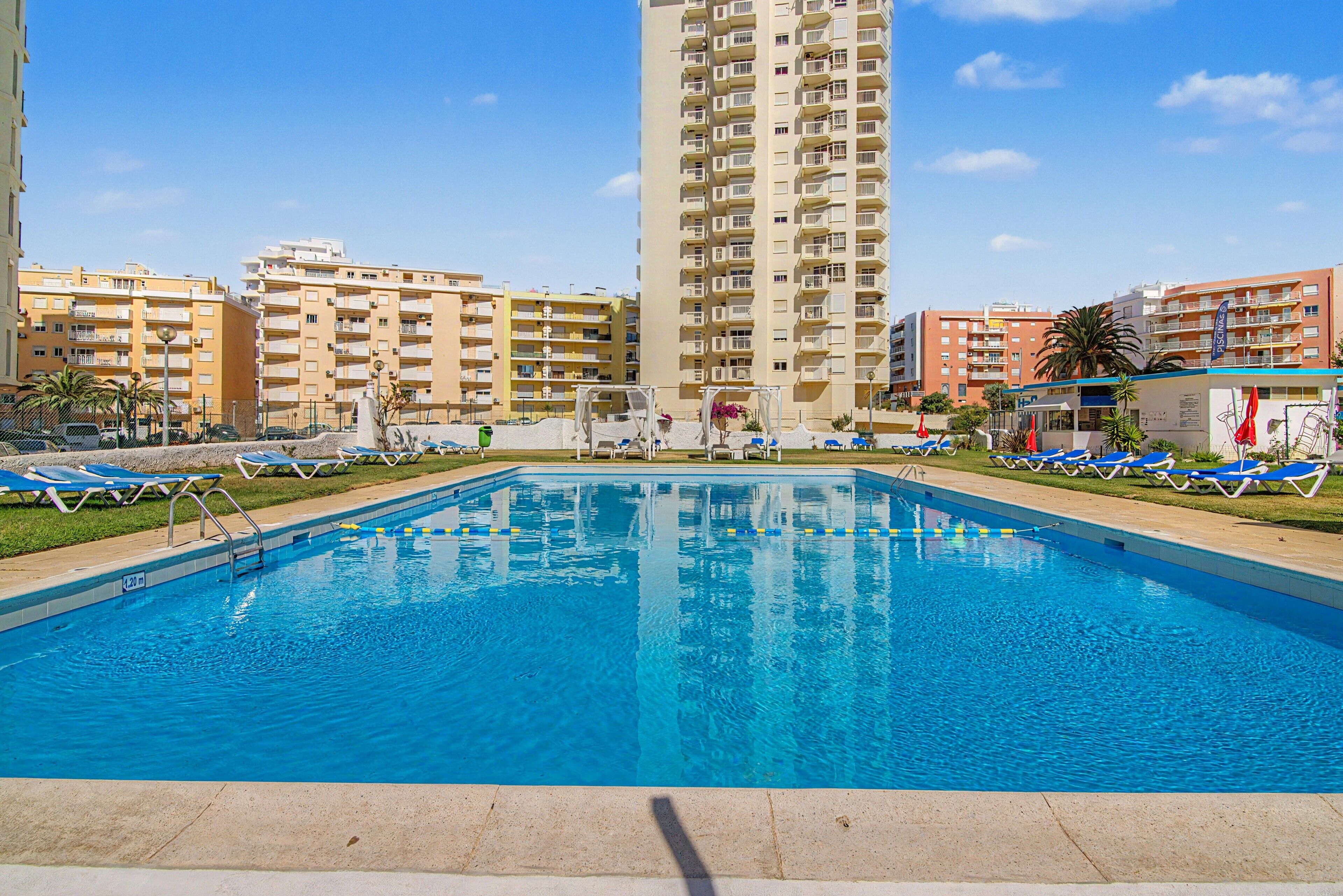 Ein Schwimmbecken mit Liegestühlen und ein hohes Wohngebäude im Hintergrund.