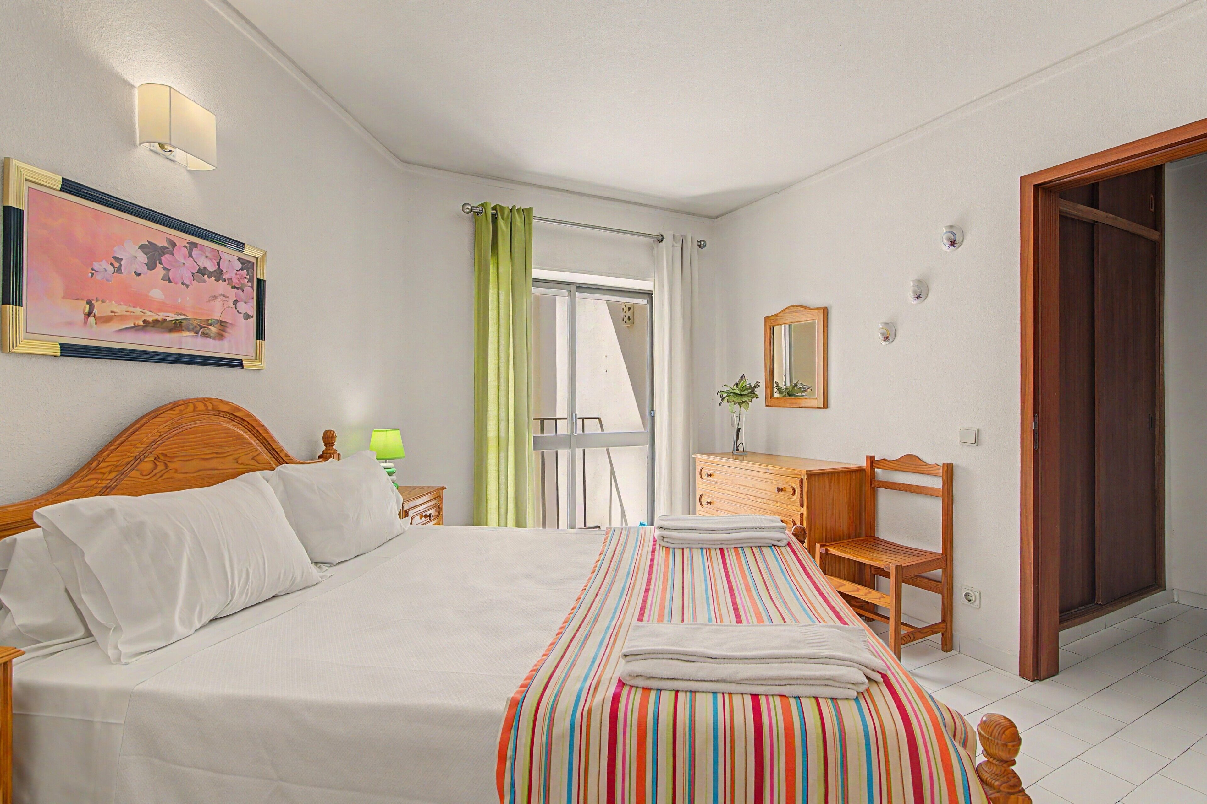 Hotelkamer met een bed, nachtkastje met lamp, stoel, raam met gordijnen en een deur.
