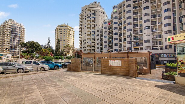 Uma área de estacionamento com vários carros, uma cerca de madeira e um edifício com varandas.