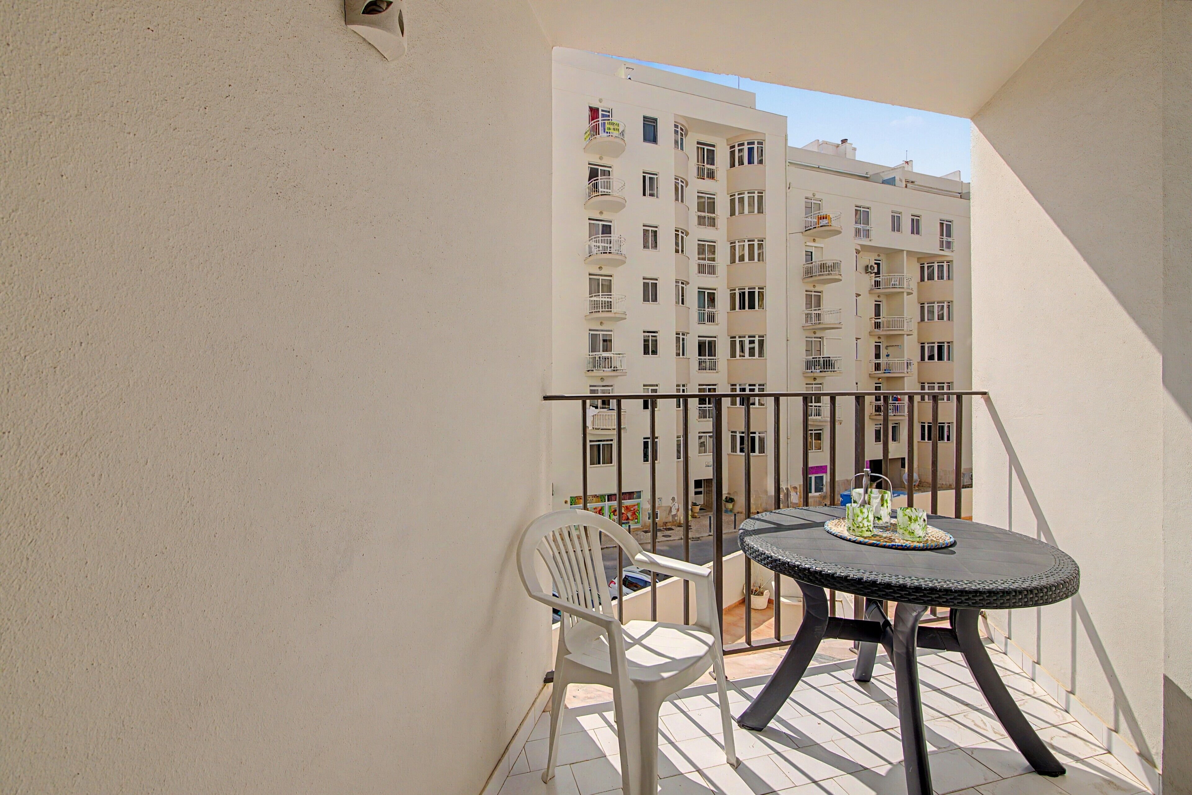 A balcony with a round table and two chairs, overlooking a street with buildings.