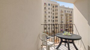 Varanda com uma mesa redonda e duas cadeiras, com vista para uma rua com edifícios.