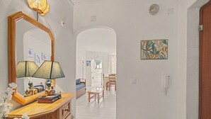 Um corredor com cômoda de madeira, espelho, abajur e um quadro na parede.