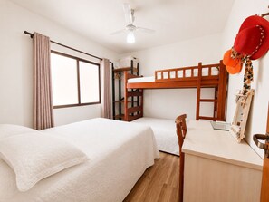 A room with bunk beds, a desk, a chair, a ceiling fan, and a window with curtains. - Residencial Itaguaçu by LikeHome (Bombinhas)