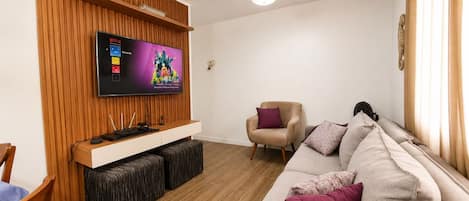 A living room with a flat-screen TV, wooden panel wall, beige sofa, and a ceiling fan.