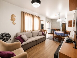 Una sala de estar con un sofá, una mesa de comedor con sillas, un ventilador y piso de madera.