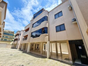 A multi-story building with balconies, a covered walkway, and a tiled ground. - Residencial Itaguaçu by LikeHome (Bombinhas)