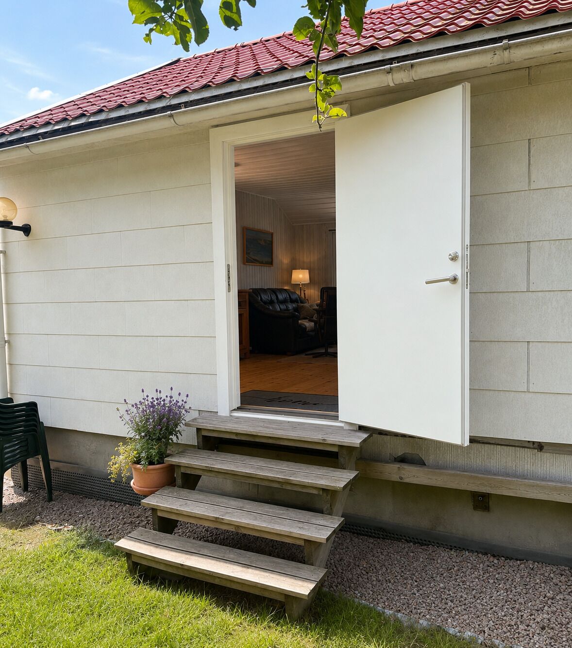 A house with a white exterior, a red-tiled roof, a wooden staircase leading to a door, a potted plant, and a bench.