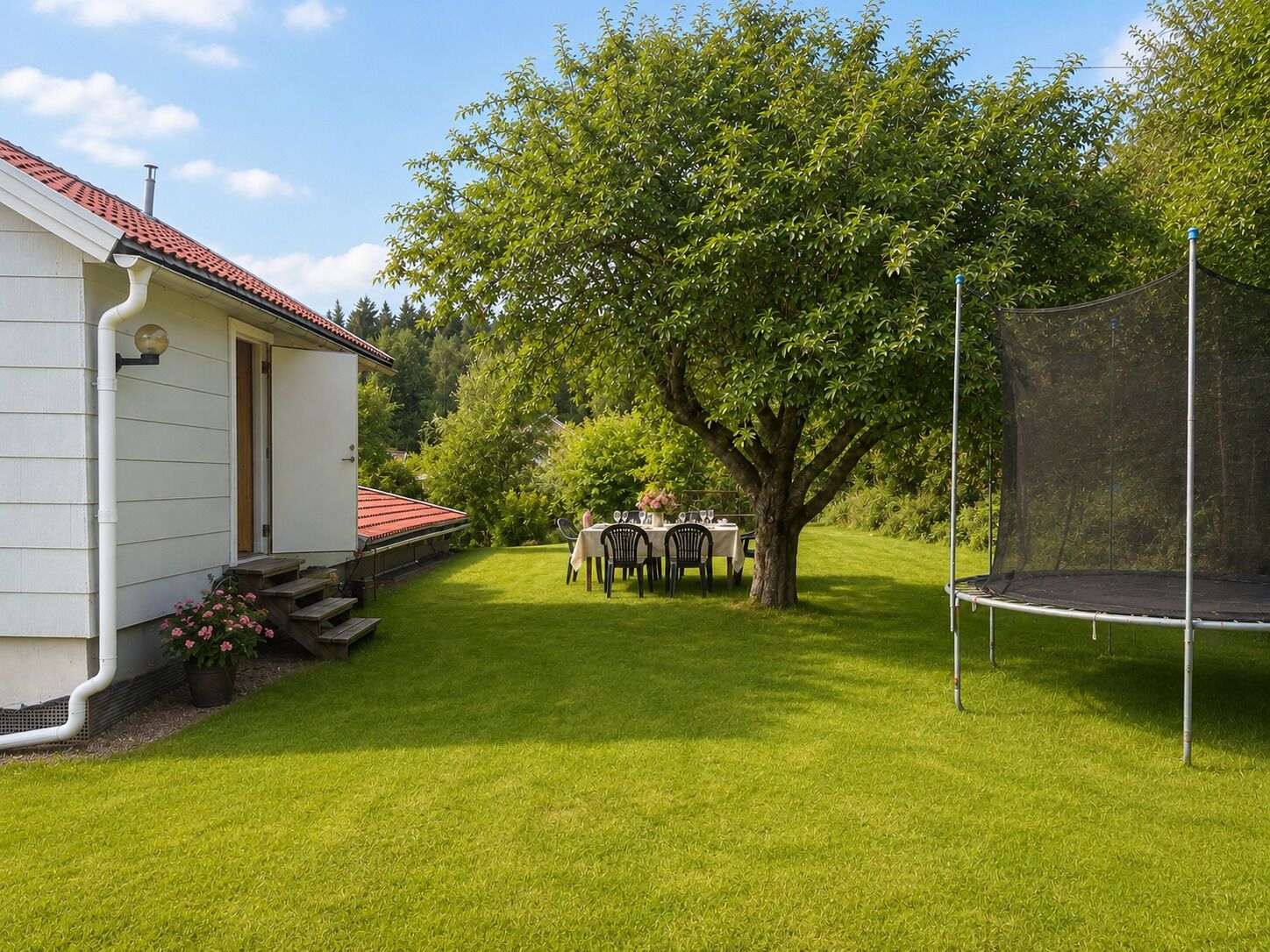 A residential property with a well-maintained lawn, a dining area with outdoor furniture, a trampoline, and a house with a red-tiled roof.
