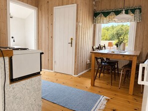 A wooden interior with a kitchen area, a dining table with chairs, and a window with a view of greenery.