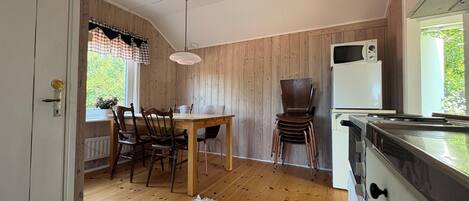 A kitchen with wooden walls, a dining table with chairs, a white refrigerator, and a stove.