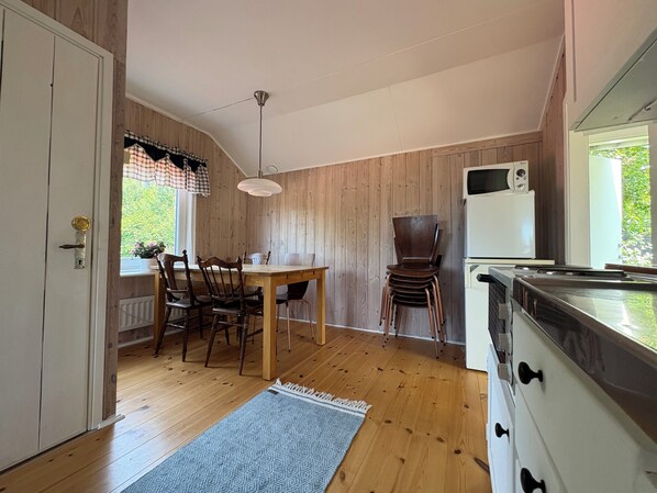 A kitchen with wooden walls, a dining table with chairs, a white refrigerator, and a stove.