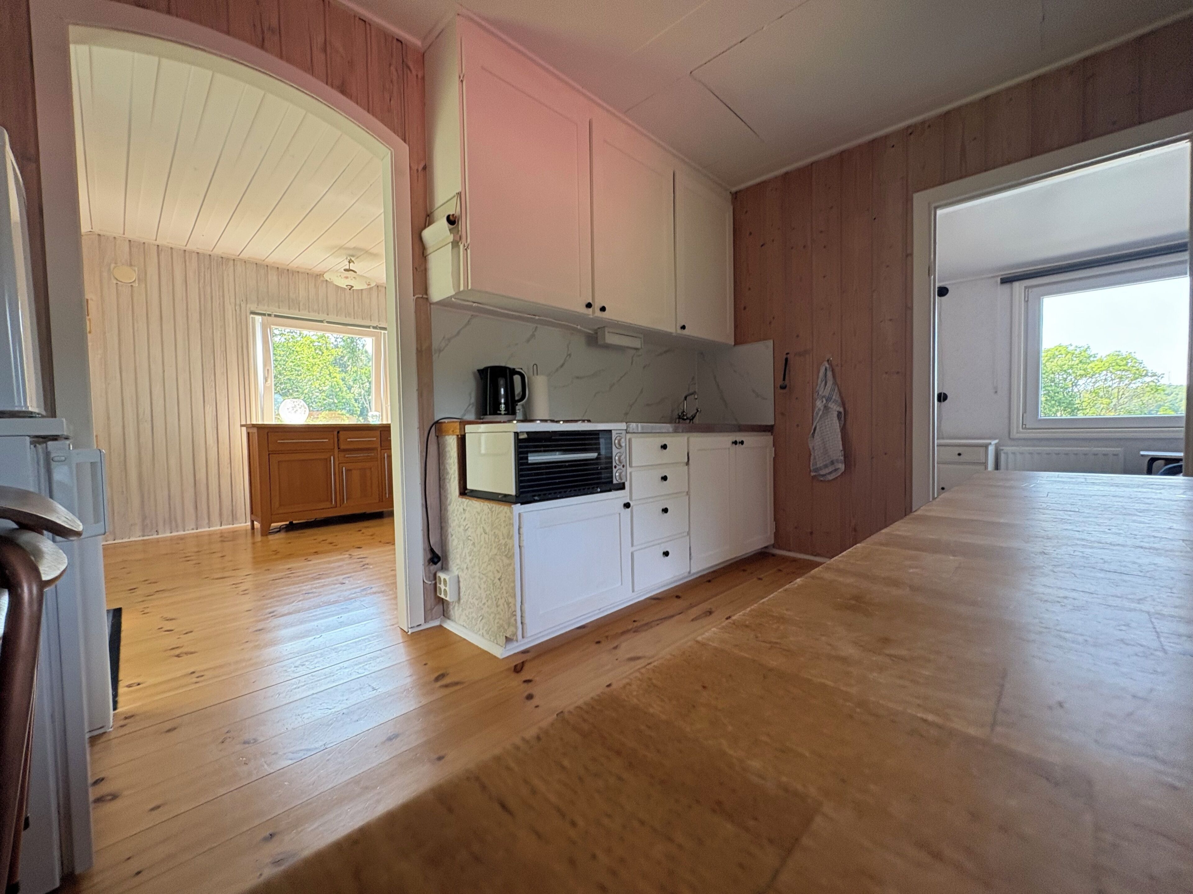 A modern kitchen with wooden flooring, white cabinets, and a large window providing natural light.