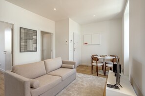 Una sala de estar moderna con un sofá color beige, una mesa de comedor con sillas, un televisor y un control remoto.