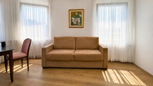 Una habitación con un sofá color beige, una mesa de comedor de madera y una silla. Hay un cuadro enmarcado en la pared.