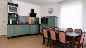 Una cocina moderna con electrodomésticos integrados, un comedor con mesa y sillas de madera, y un ventanal con cortinas ligeras.