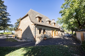 A stone house with a steeply pitched roof, multiple windows, and a paved driveway. - Bellevue Guest Rooms - Room 3 (Junhac)