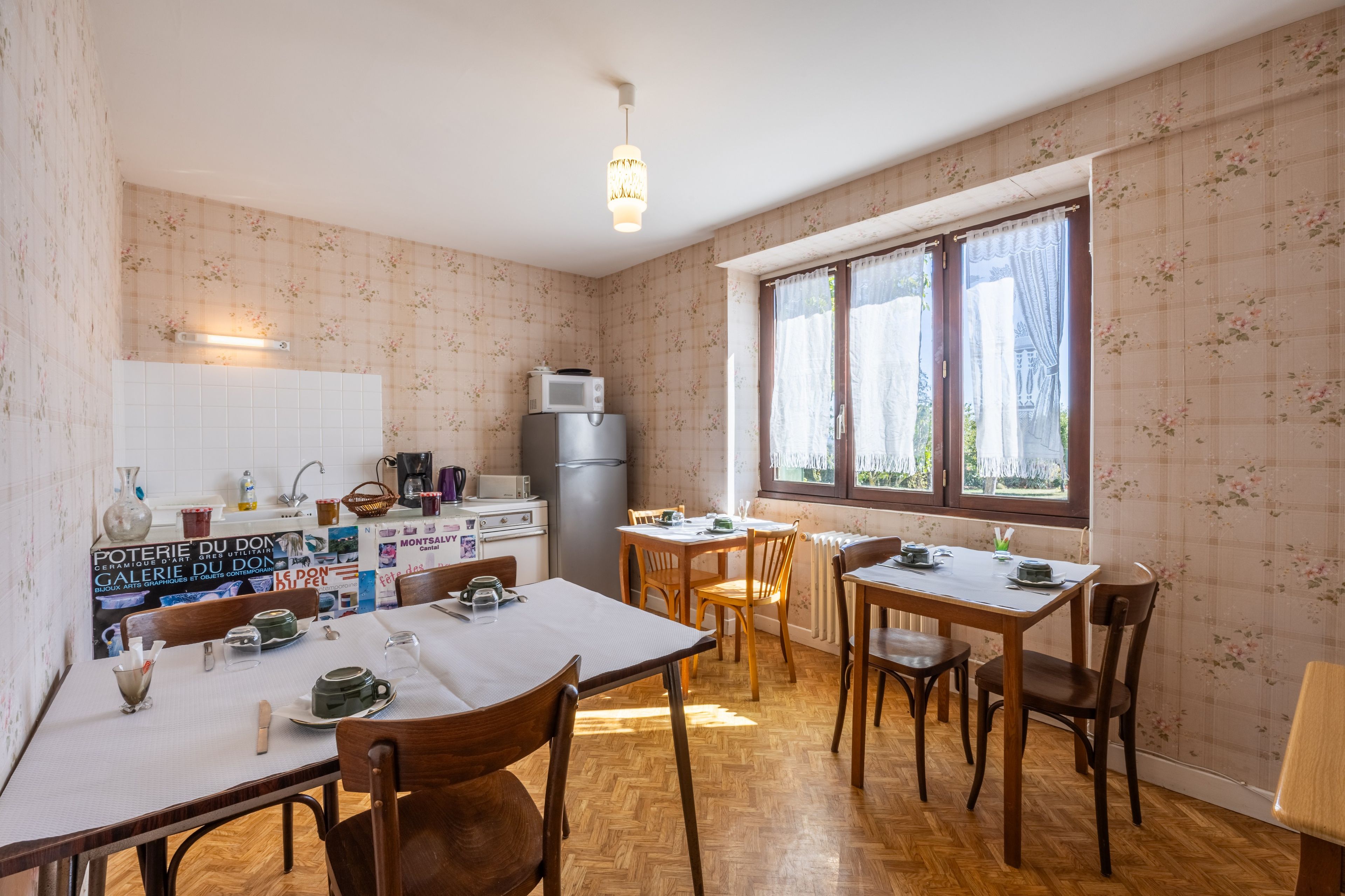 A dining area with a table set for four, a refrigerator, and a microwave.