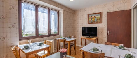 A dining area with two tables, chairs, a television, and a painting on the wall.