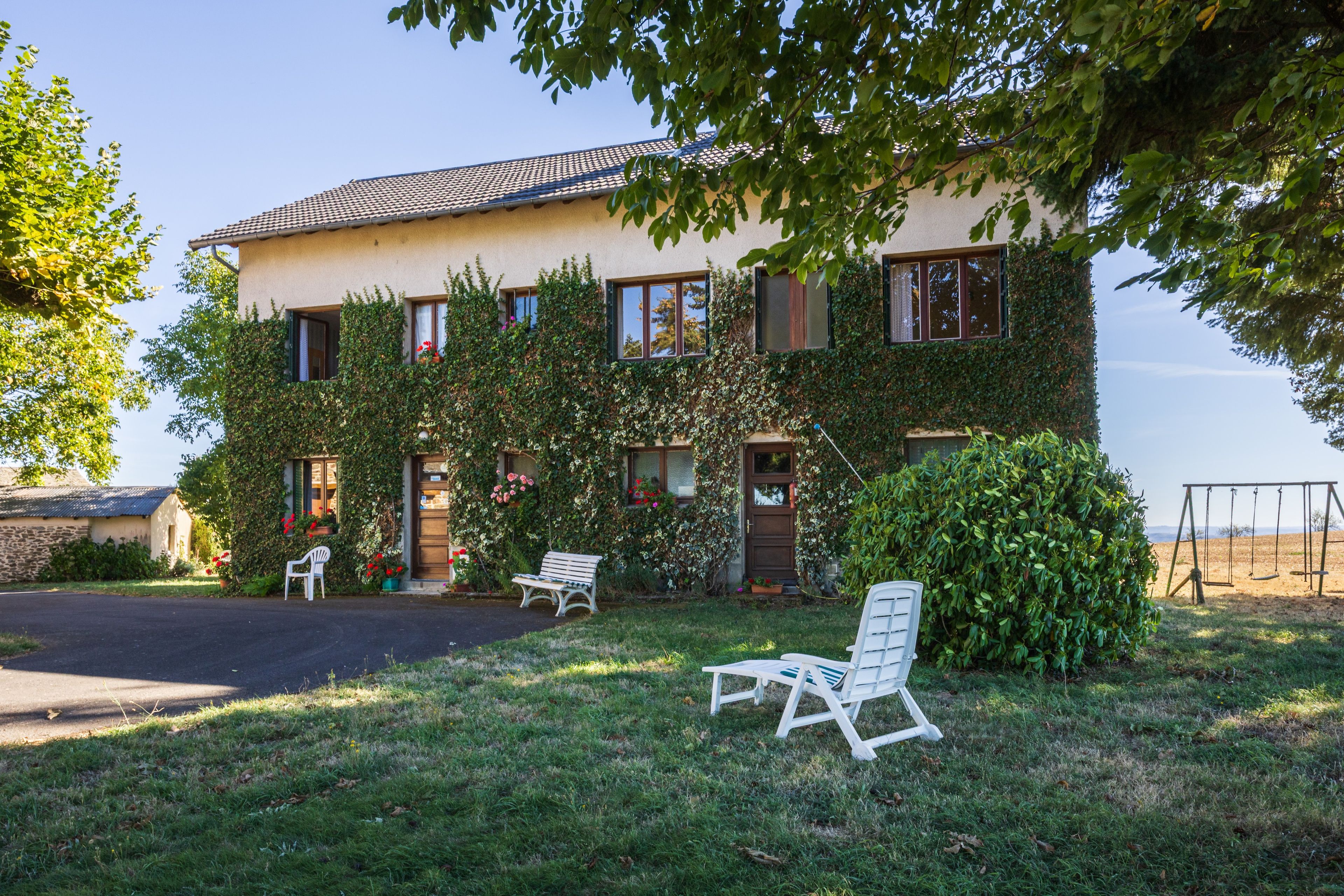 Une maison à deux étages avec un jardin, une balançoire et un espace salon extérieur.