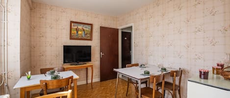 A dining area with a table set for two, a television, and a door leading to another room.