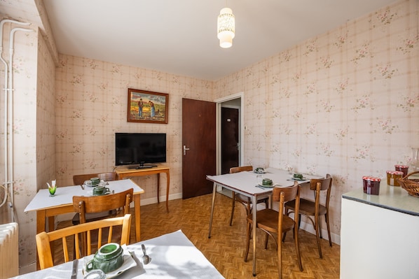 A dining area with a table set for two, a television, and a door leading to another room.