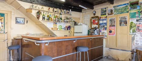A bar area with stools, a refrigerator, and various bottles and glasses.