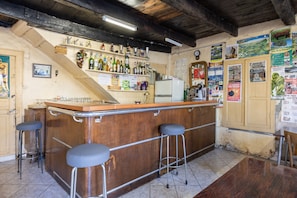 Una zona de bar con taburetes, un refrigerador y varias botellas y vasos.