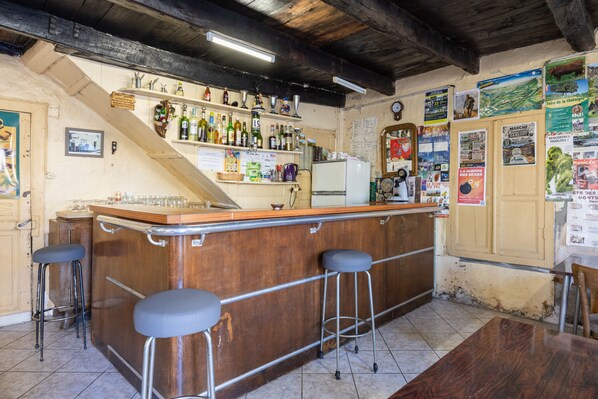 A bar area with stools, a refrigerator, and various bottles and glasses.