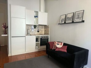 A compact living space with a kitchenette, a black sofa with cushions, and a grey rug. - Charm in Porto, located in the heart of Porto's most famous street (Porto)