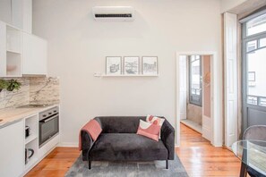 Ein modernes Wohnzimmer mit einem dunkelgrauen Sofa, einer Marmor-Spritzschutzwand in der Küche und einem großen Fenster.