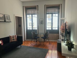 A living room with a black sofa, two chairs, a glass table, and a potted plant. - Charme in Porto, located in the heart of Porto’s most iconic street. (Porto)