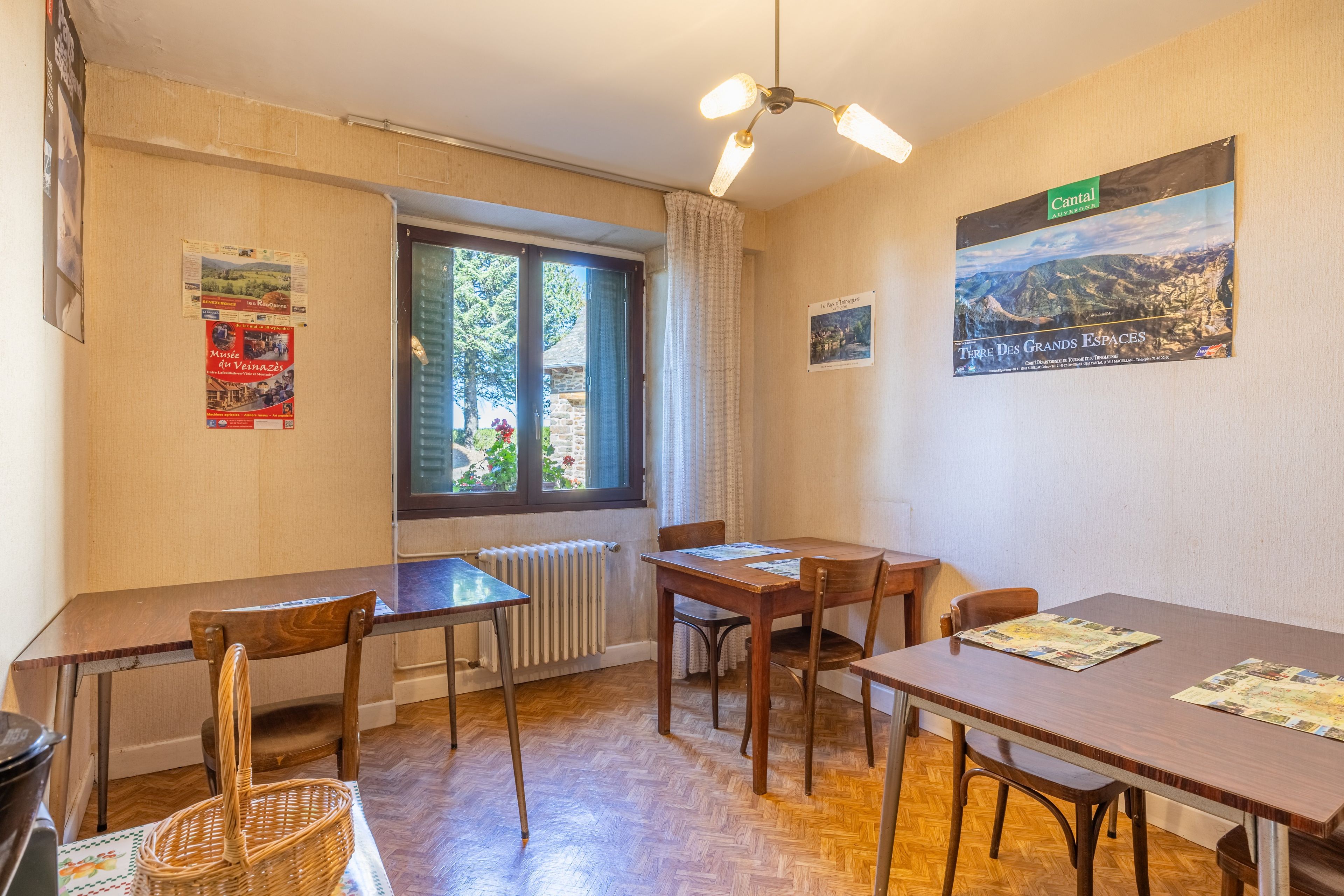 Un comedor con mesas y sillas de madera, una ventana con vista a follaje y un ventilador de techo.