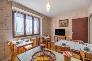 A dining area with two tables, chairs, a television, and a painting on the wall.