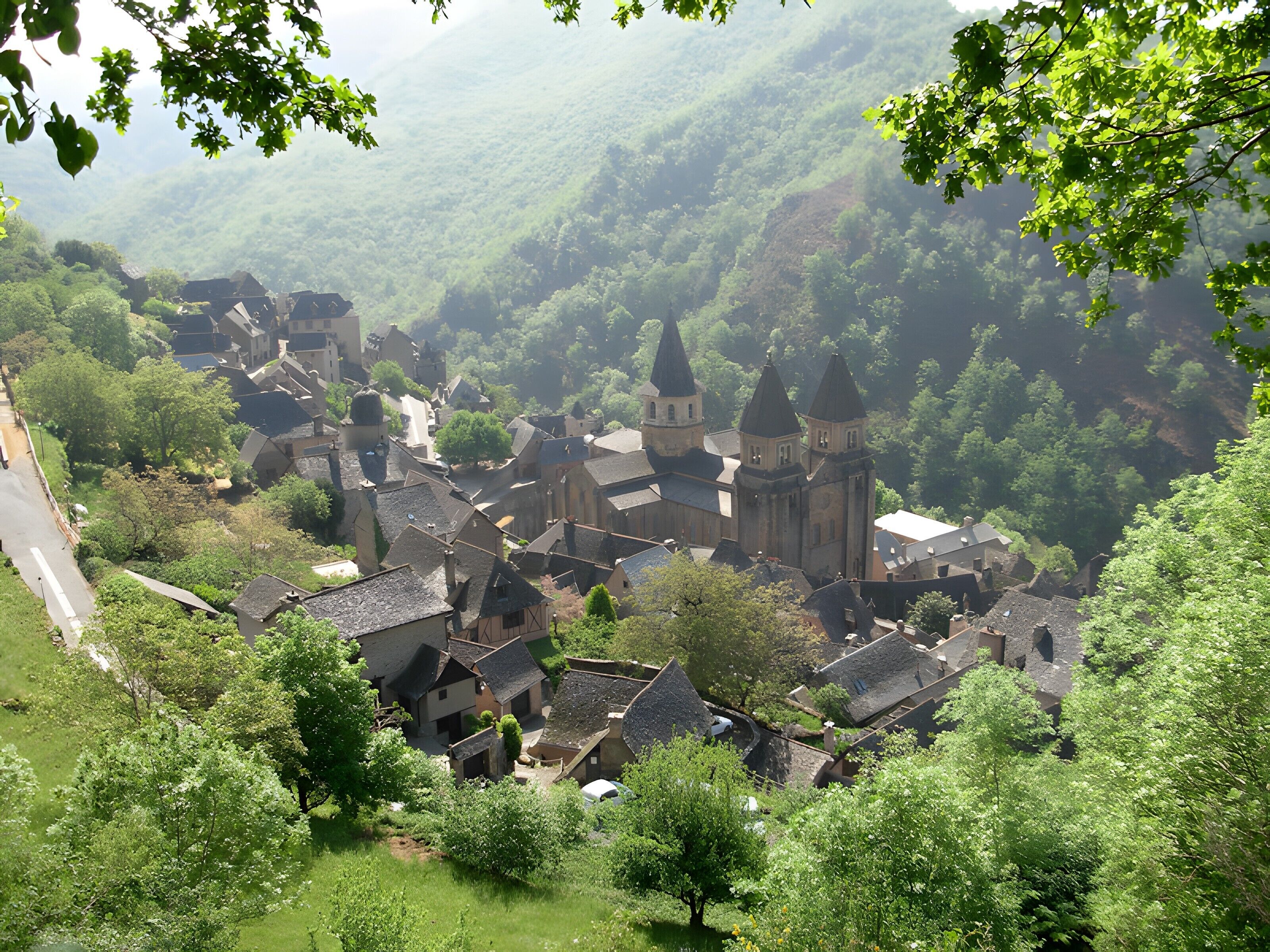 A village with traditional architecture, including a prominent church with towers, surrounded by lush greenery and a valley.