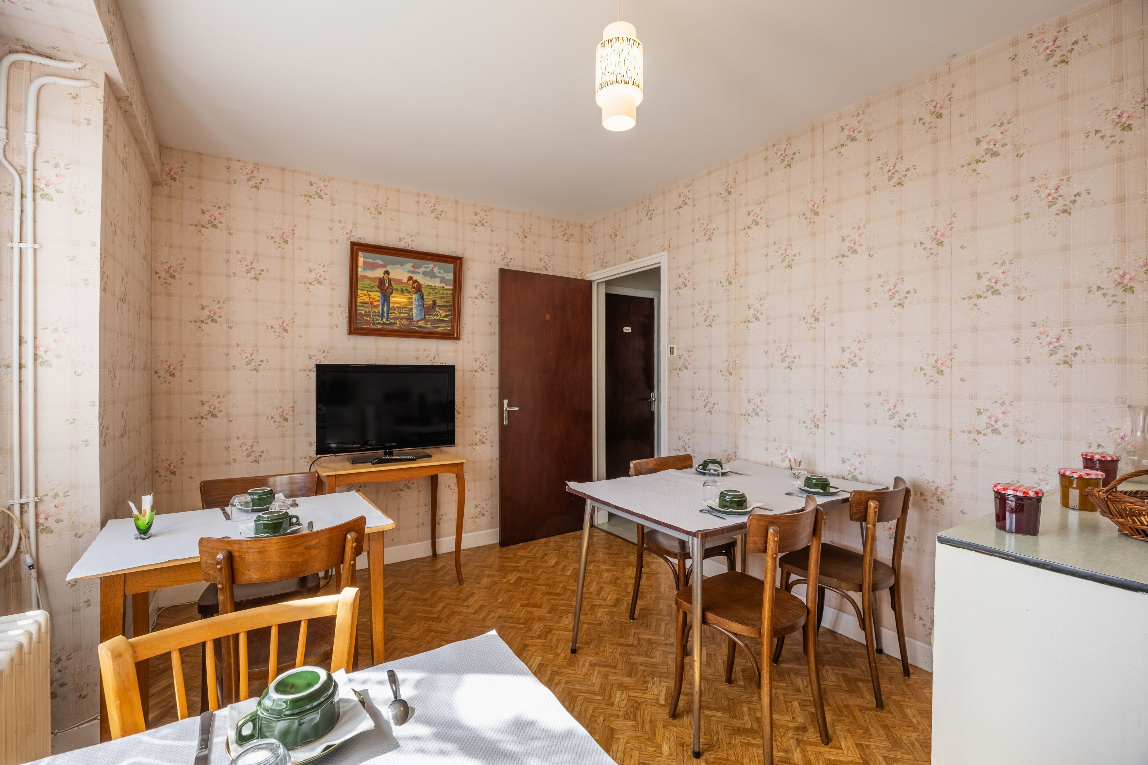 A dining area with a table set for two, a television, and a door leading to another room.