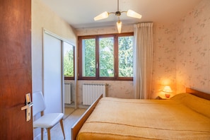 Een slaapkamer met een bed, een stoel, een raam met gordijnen en een radiator.