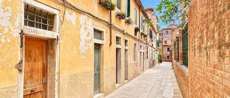 A narrow street with buildings on either side, featuring wooden doors and windows with shutters.