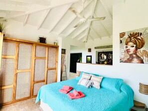 A bedroom with a large bed, a ceiling fan, a rattan wardrobe, and a painting on the wall. - Villa Atlantide – 3 BR Hillside with Ocean View & Infinity Pool (Las Terrenas)