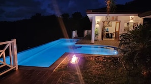 A swimming pool with a fire feature, a covered outdoor seating area, and a view of a house with a well-lit entrance. - Villa Atlantide – 3 BR Hillside with Ocean View & Infinity Pool (Las Terrenas)