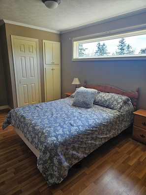 Un dormitorio con cama, suelo de madera, armario y ventana con vistas.