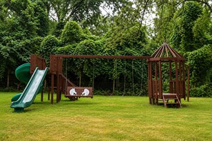 A playground with a slide, swings, and a wooden playhouse.