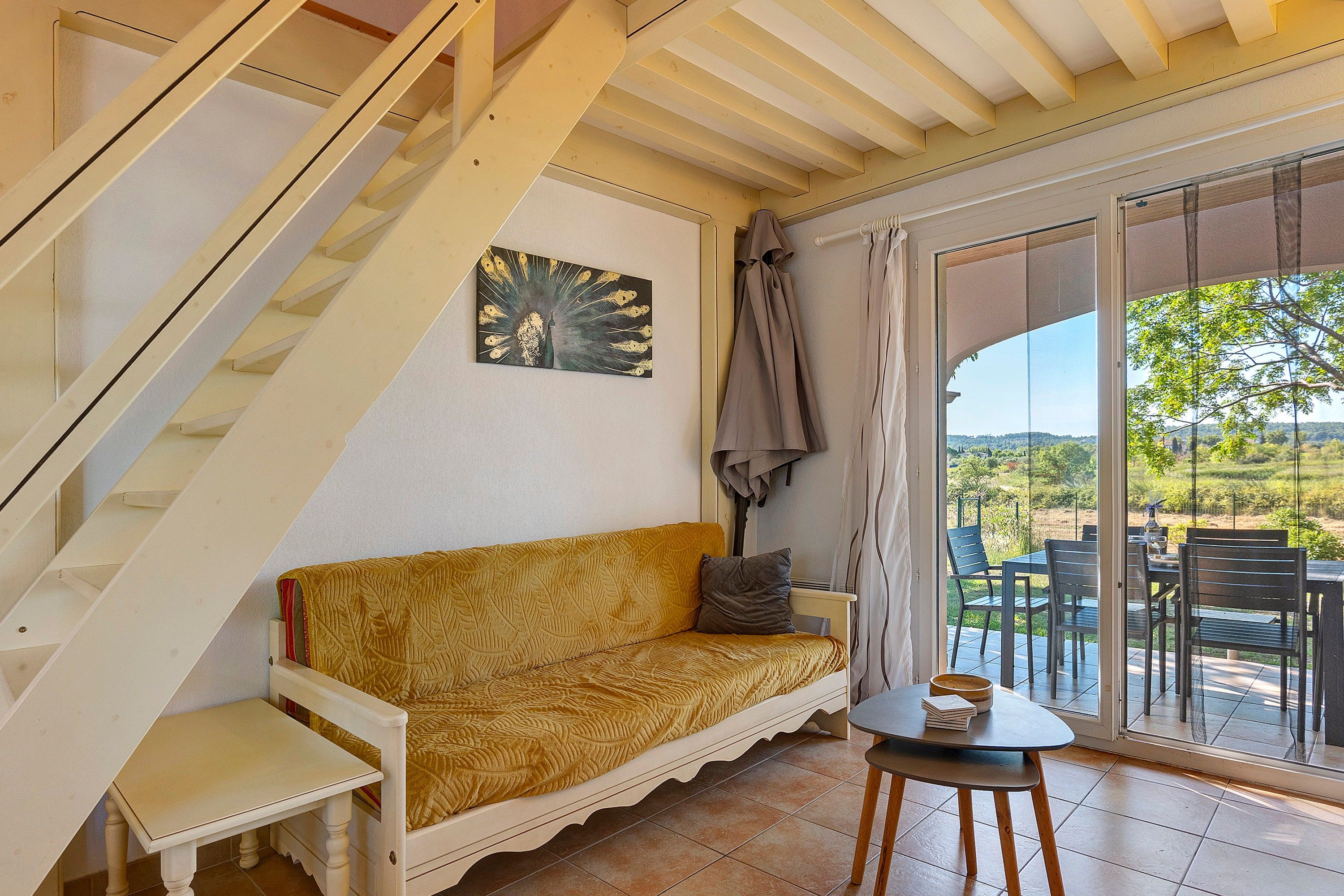 Ein Zimmer mit Treppe, einer Couch, einem kleinen Tisch und Blick ins Freie.