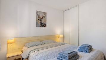Ein Schlafzimmer mit Bett, Kissen, einem Nachttisch, einer Wandlampe, einem Gemälde und einem Kleiderschrank.