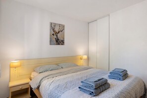 Un dormitorio con cama, almohadas, mesita de noche, lámpara de pared, un cuadro y un armario.